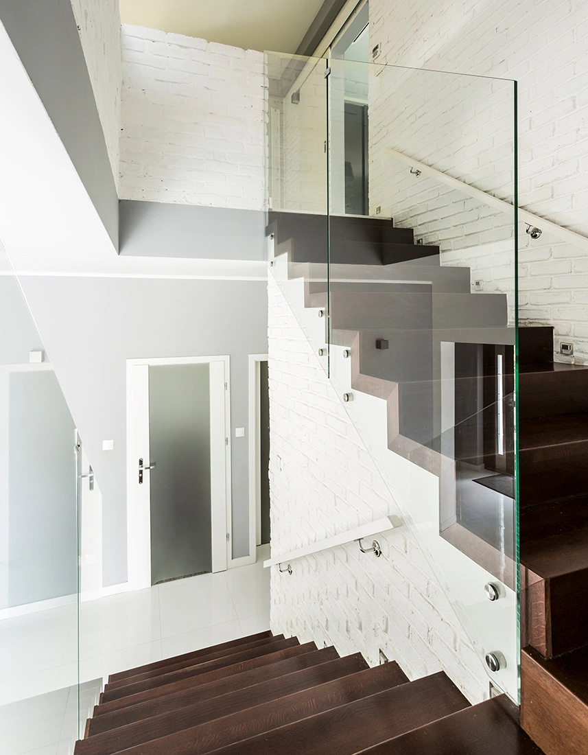 ciemne nowoczesne schody dywanowe ze szklaną balustradą i białymi poręczami