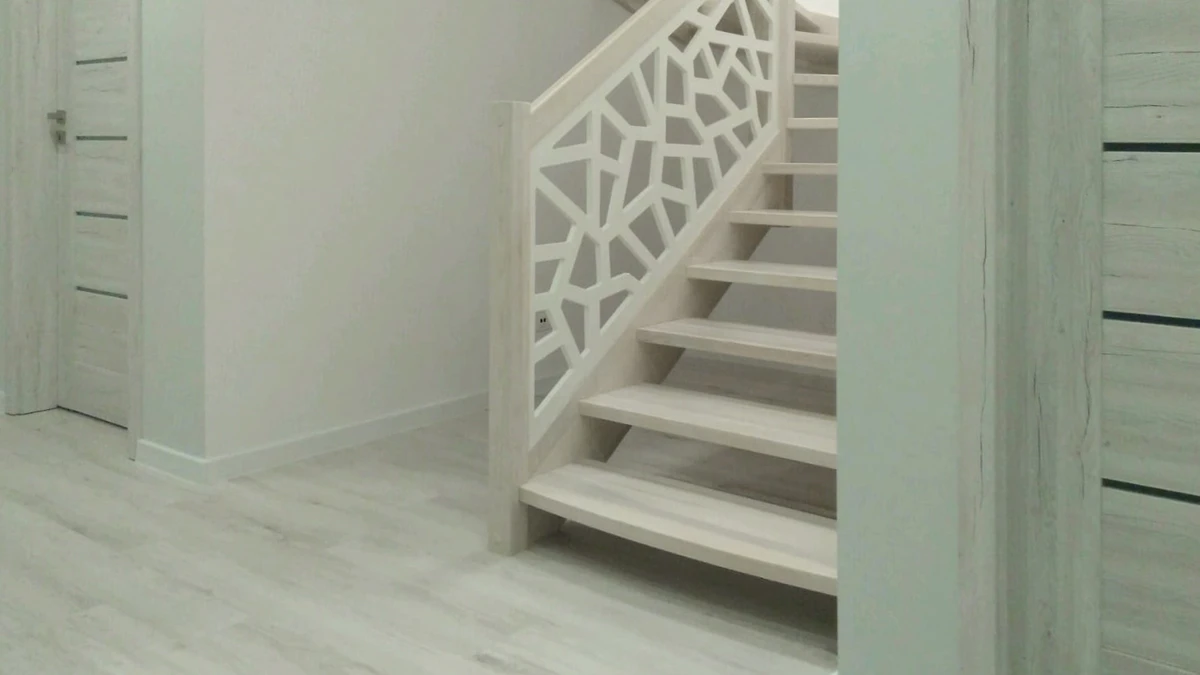 jasne schody jesionowe z białą ażurową balustradą w geometryczne wzory